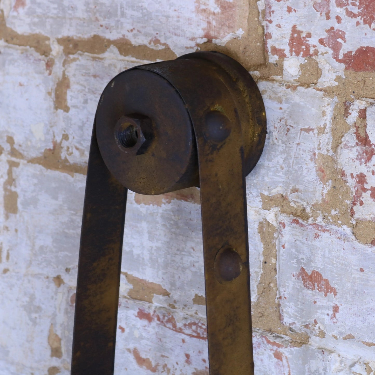 Rust-colored metal pulley system on a textured wall background
