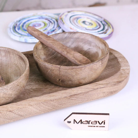 Wooden bowls and a spoon on a wooden tray with colorful coasters in the background, featuring the Maravi brand.