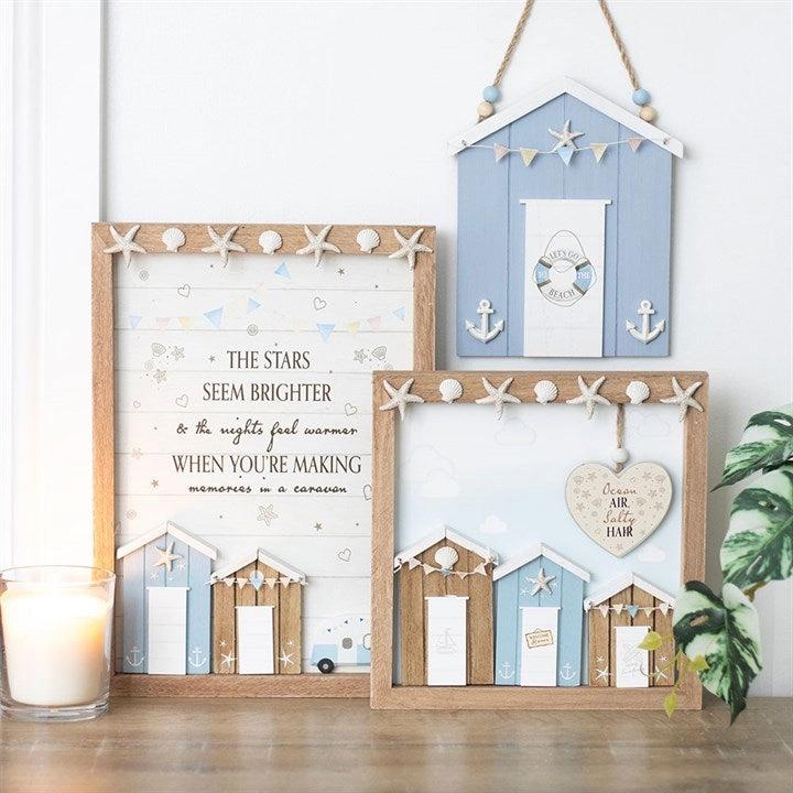Decorative wall art with beach hut designs and text on a wooden surface.
