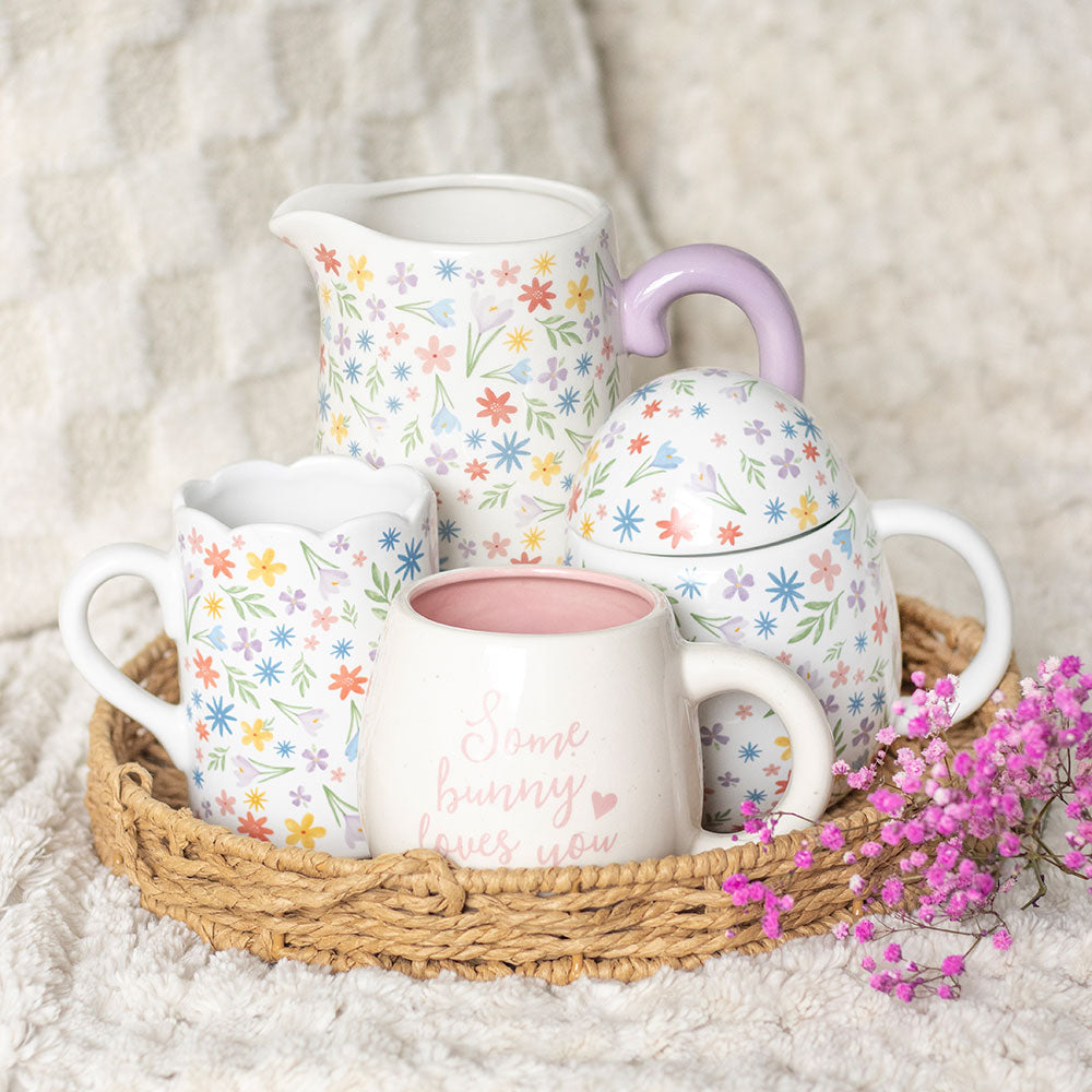 Tea set with floral patterns on a woven tray with pink flowers on a soft surface