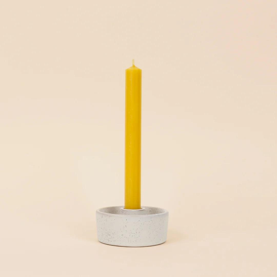Yellow candle in a gray ceramic holder on a beige background