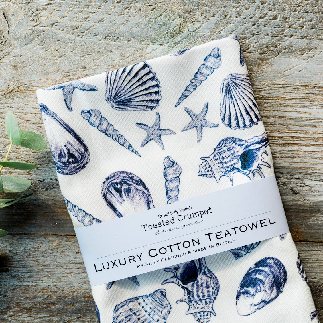 Folded luxury cotton teatowel with shell pattern on a wooden surface