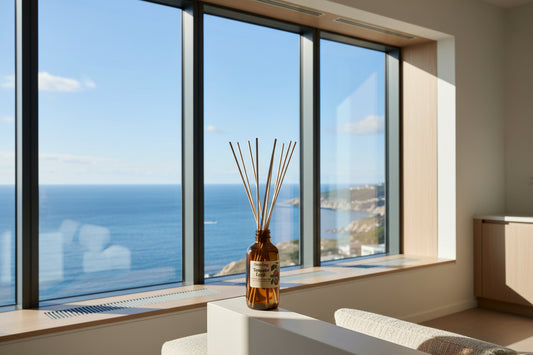 An amber glass reed diffuser bottle with a white label reading 'Oneology Tomato Leyf' and multiple natural reed sticks, displayed on a white pedestal against a warm beige background.