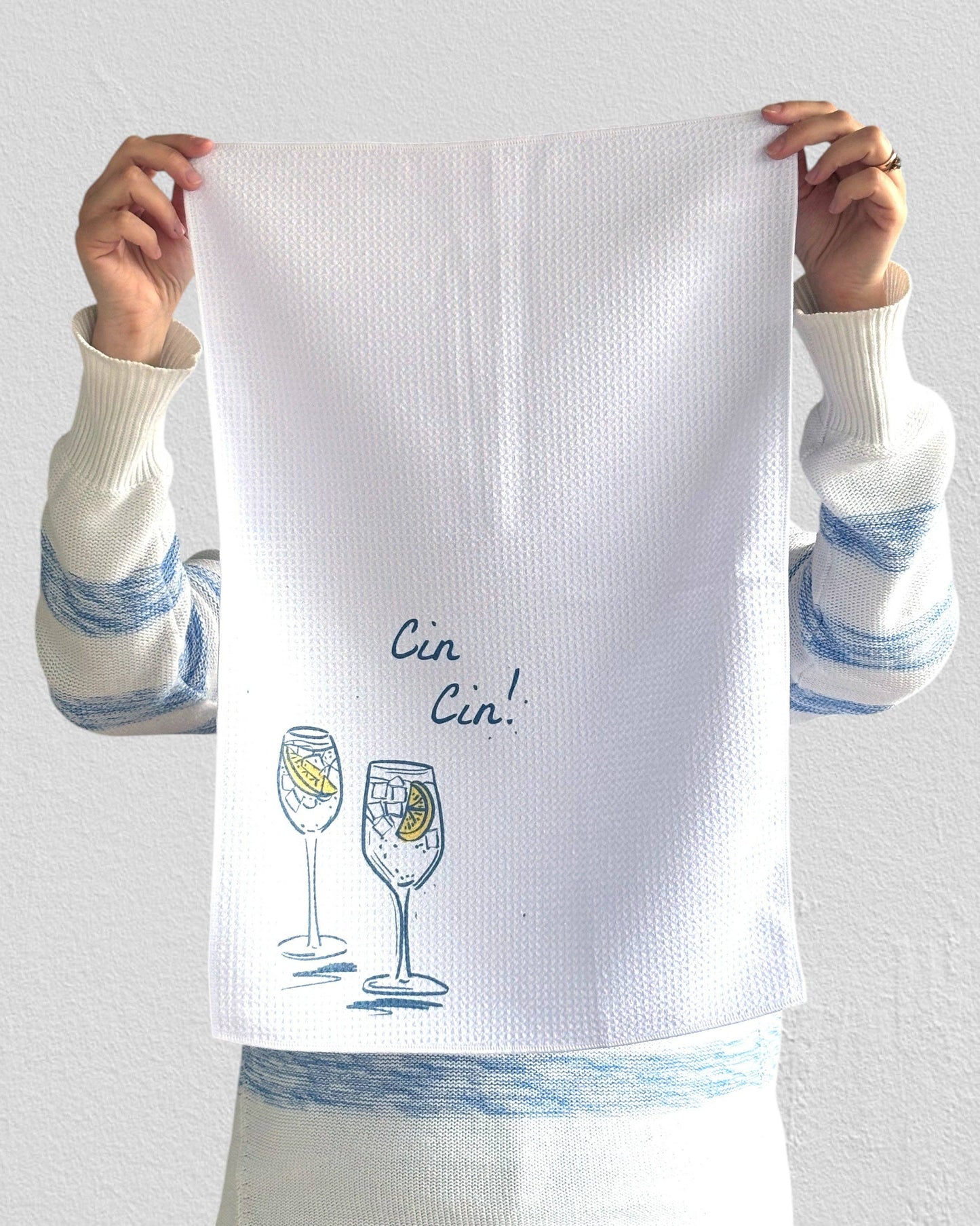 Person holding a white towel with 'Cin Cin!' and wine glass designs.