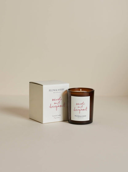 A Plum & Ashby 'melt and deeproot' scented candle in an amber glass jar next to its cream-colored packaging box, set against a warm beige background.