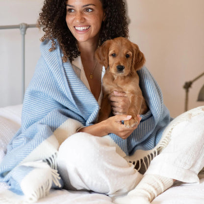 Woman holding a puppy wrapped in a blue blanket on a bed
