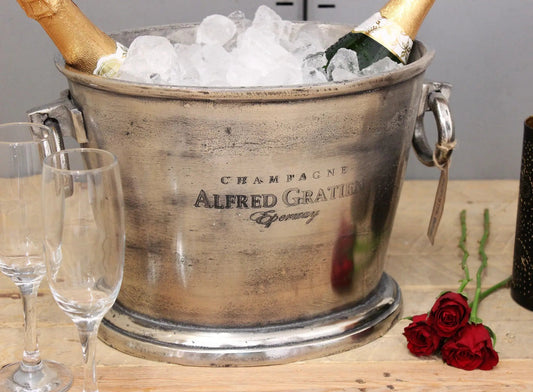 Vintage champagne bucket with ice and champagne bottles, accompanied by glasses and roses on a wooden surface.