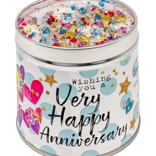 A tin candle with a 'Happy Anniversary' message, decorated with colorful confetti-like sprinkles and heart shapes.