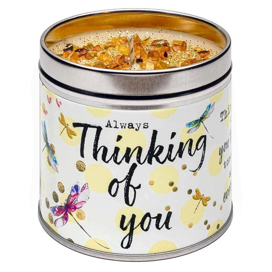 A tin candle with a floral and butterfly pattern, labeled 'Thinking of you', with a lit wick inside.