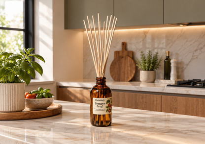 A reed diffuser bottle with a label reading 'Tomato Leaf' sits on a marble kitchen counter, surrounded by kitchen plants and wooden cabinetry in the background.