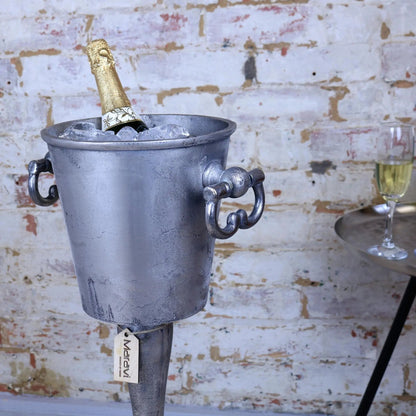Metal ice bucket with a bottle of champagne against a brick wall.