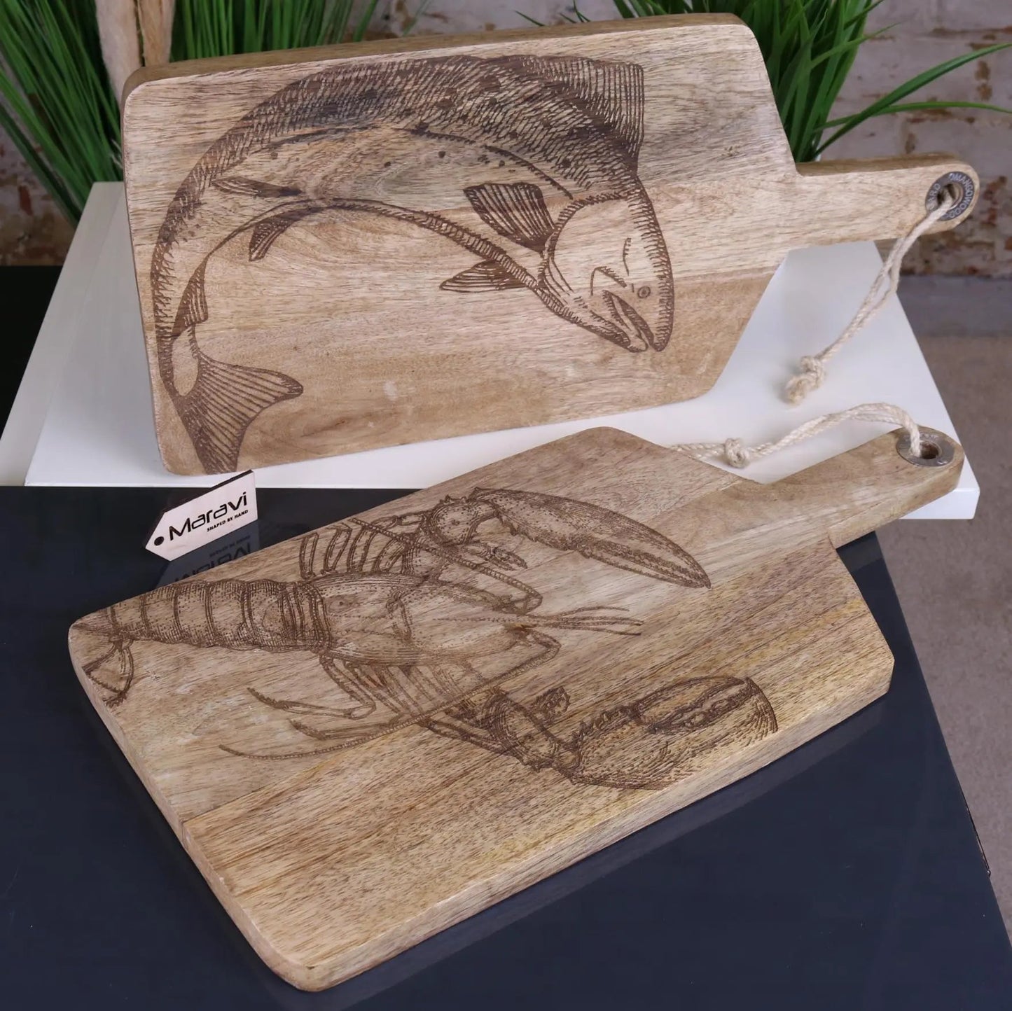 Two wooden cutting boards with engraved fish and lobster designs on a white surface.