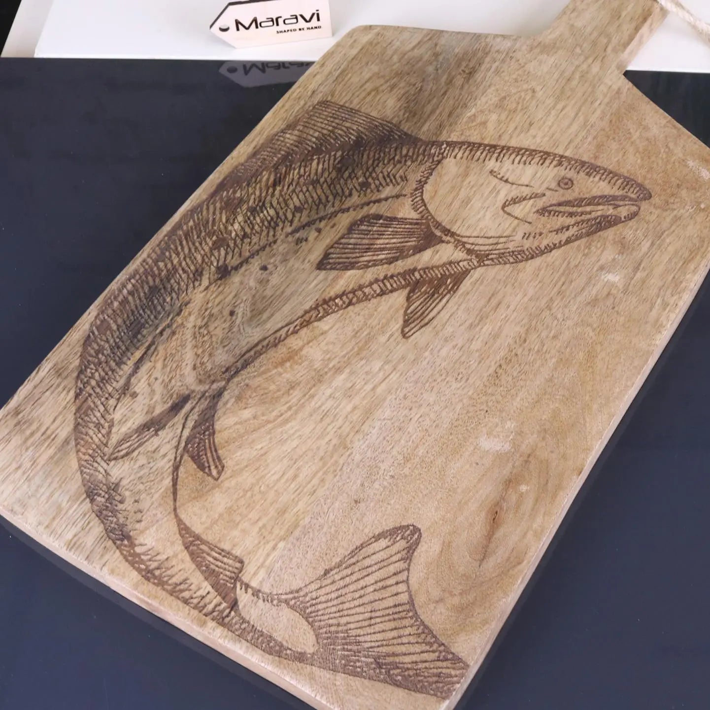 Wooden cutting board with engraved fish design on a dark surface