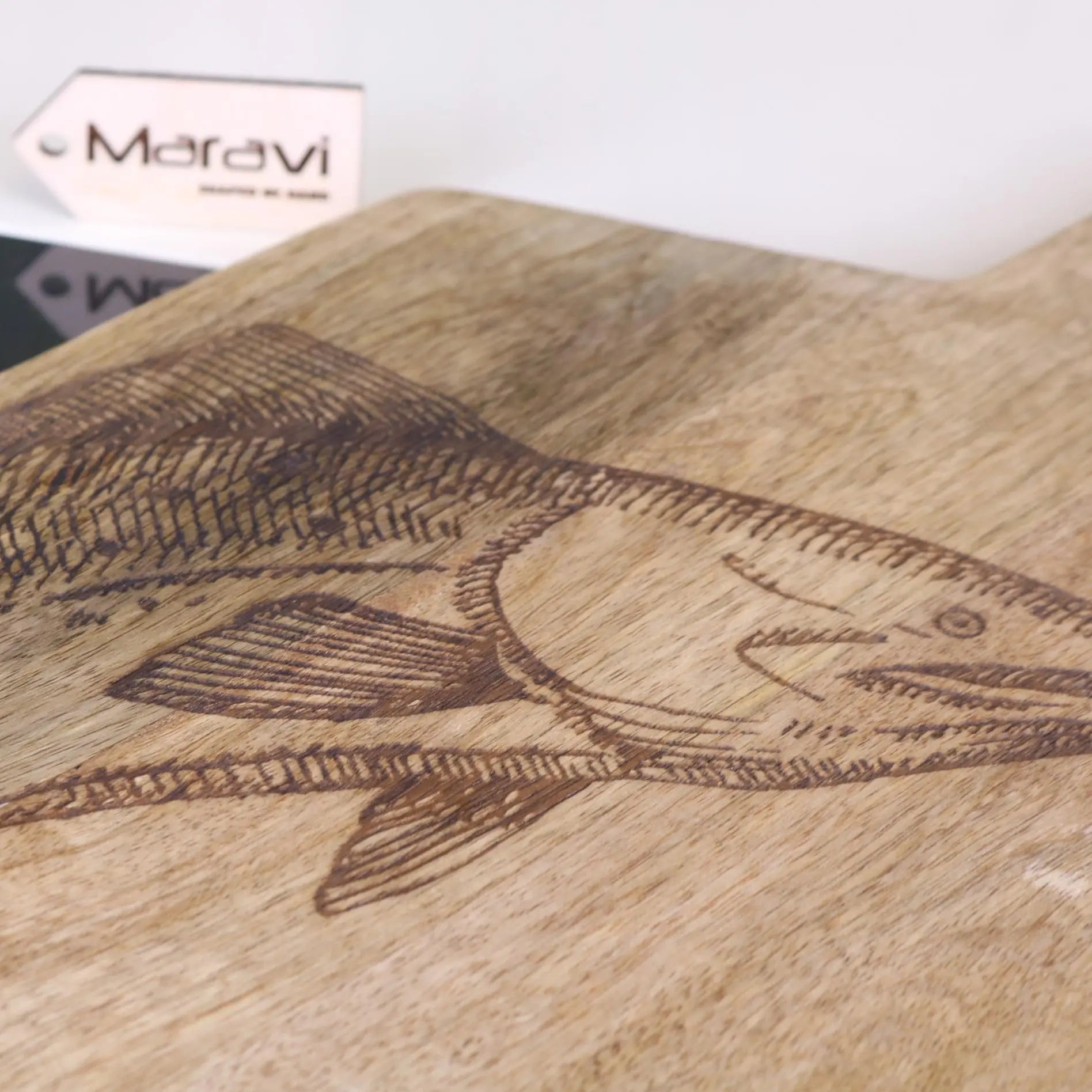 Wooden cutting board with engraved fish design and Moravi brand logo in the background.