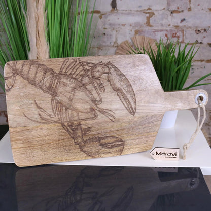 Wooden cutting board with lobster design on a white surface with plants in the background