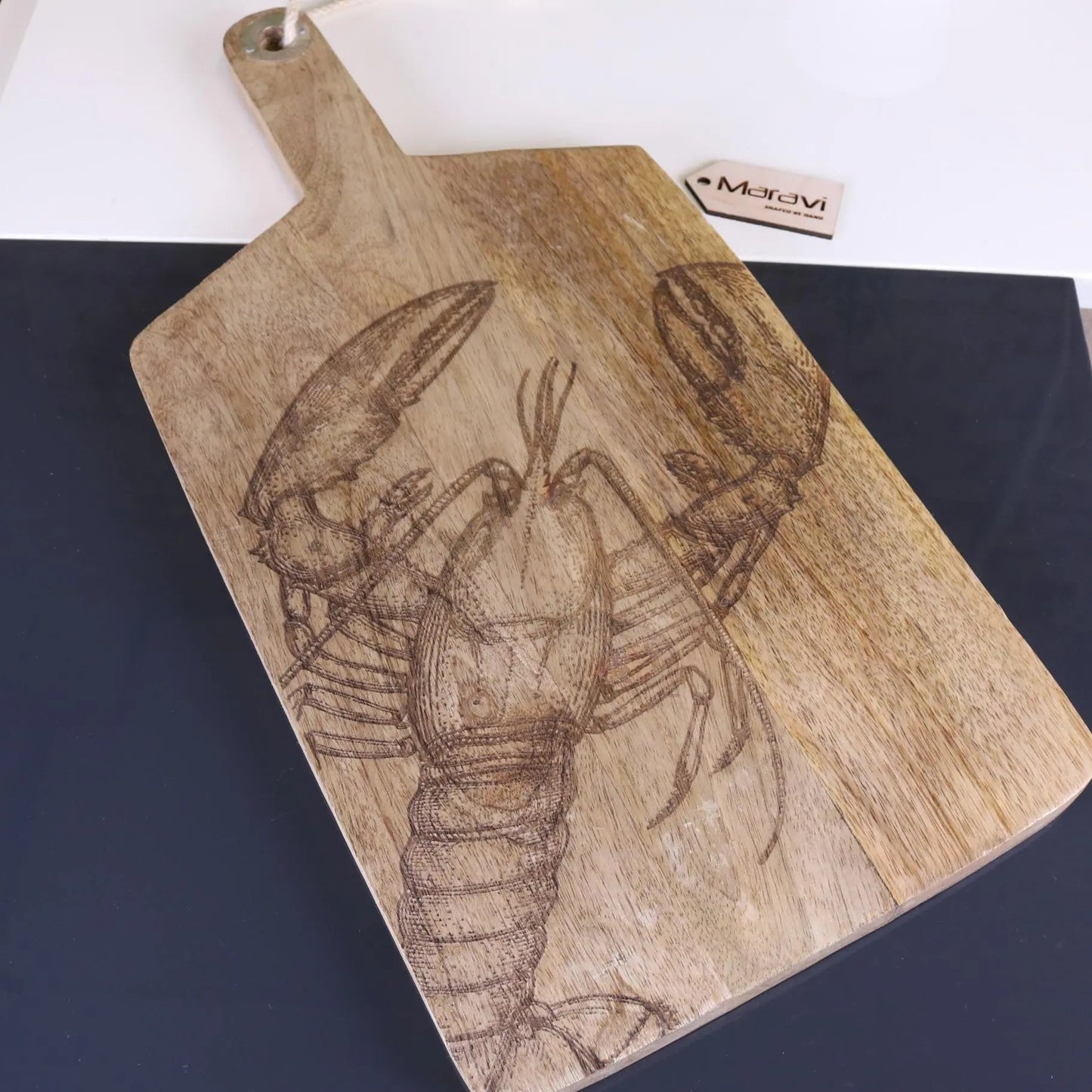 Wooden cutting board with a engraved lobster design on a white surface.