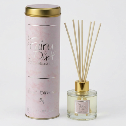 Fairy Dust reed diffuser set by Candle Flame, featuring a tall light pink marble-patterned cylindrical packaging container with a gold lid next to a clear glass bottle with a gold cap, beige reeds, and a matching pink label.