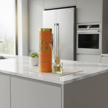 An orange cylindrical perfume bottle with gold accents stands on a marble countertop in a modern kitchen, next to a reed diffuser with gold accents.