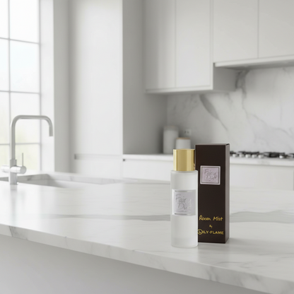A bottle of Dalyl Flame Room Mist with a gold cap stands next to its dark brown box on a white marble kitchen counter in a bright, modern kitchen.