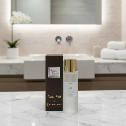 A bottle of Fairy Dust Room Mist by LILY-FLAME stands next to its dark brown box on a white marble countertop, with a blurred modern bathroom in the background.