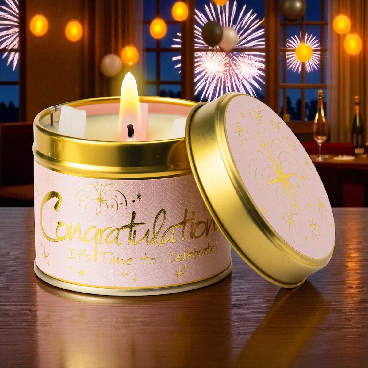 Lit candle in a 'Congratulations' tin with fireworks in the background