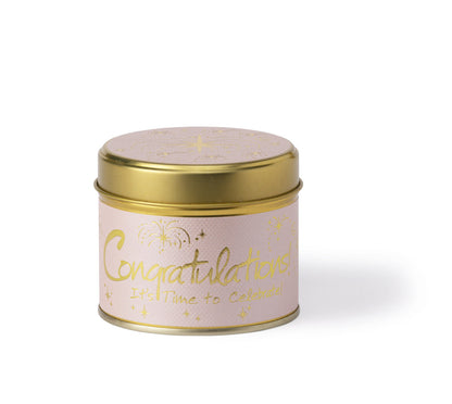 A round metal tin candle with a gold lid and base, featuring a light pink label with gold foil text that reads 'Congratulations! It's Time to Celebrate' along with gold firework and star illustrations, set against a plain white background.