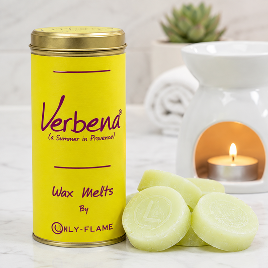 A yellow tin of ONLY-FLAME Verbena Wax Melts by ONLY-FLAME stands on a light marble surface with several pale green wax melts in front and a white scented candle holder with a lit tealight in the background.
