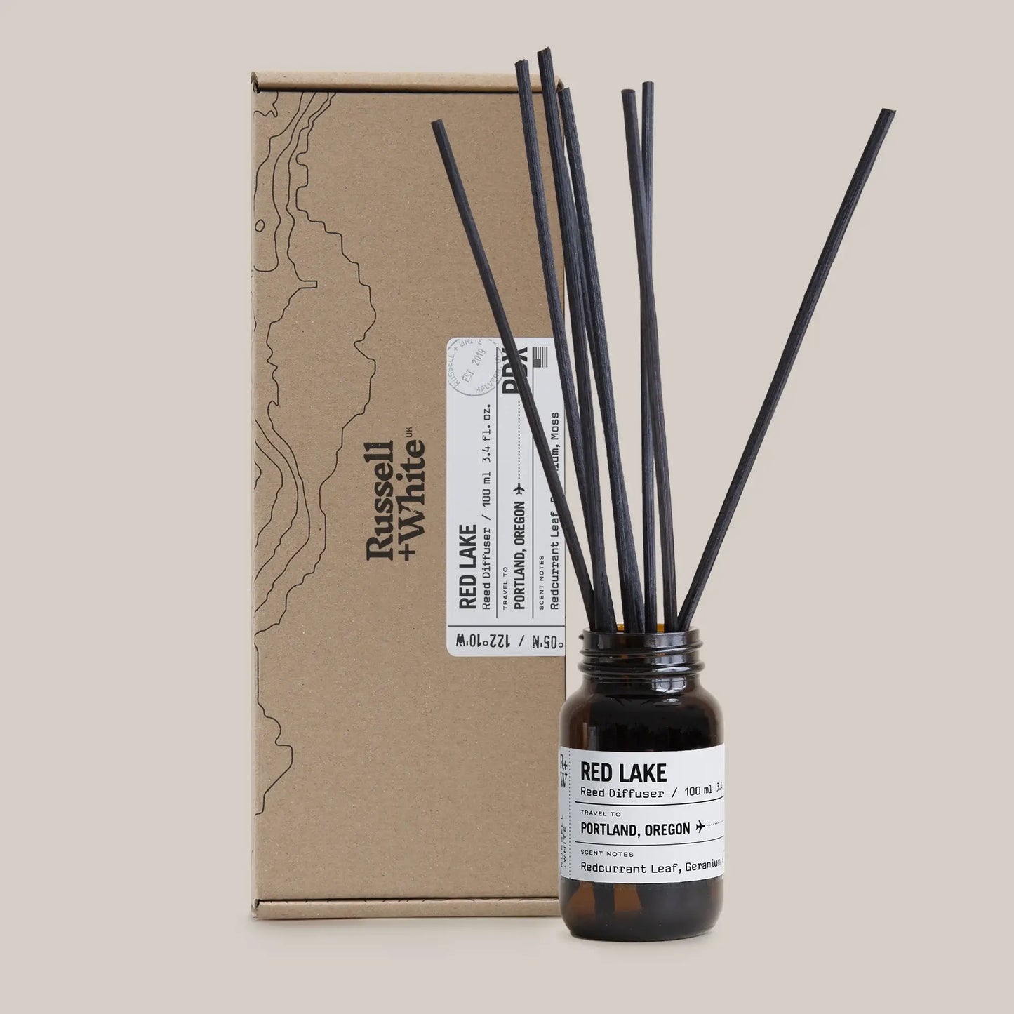 Reed diffuser with black sticks and a brown cardboard box on a beige background