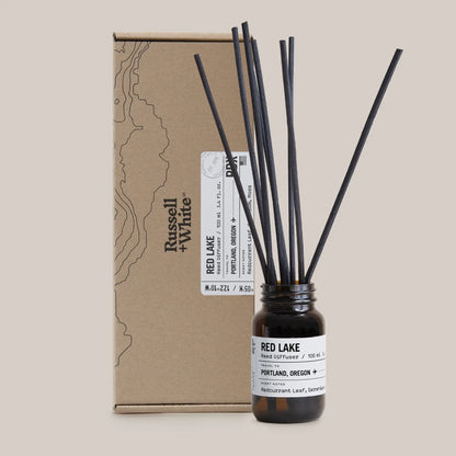 Reed diffuser with black sticks and a brown cardboard box on a beige background