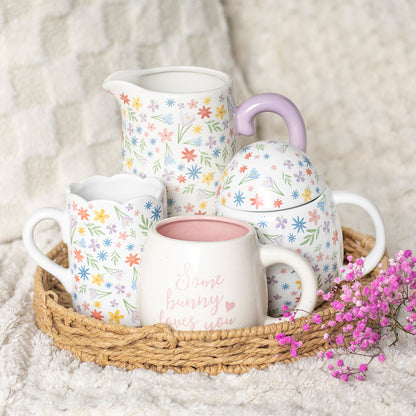 Tea set with floral patterns on a woven tray with pink flowers on a soft surface