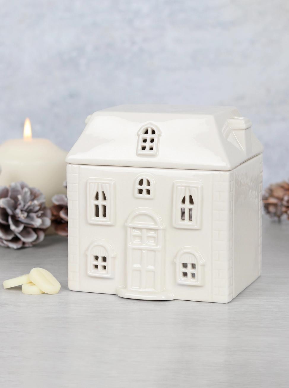 White ceramic house-shaped lantern with a candle inside on a light gray background
