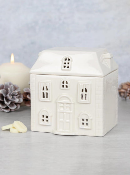 White ceramic house-shaped lantern with a candle inside on a light gray background