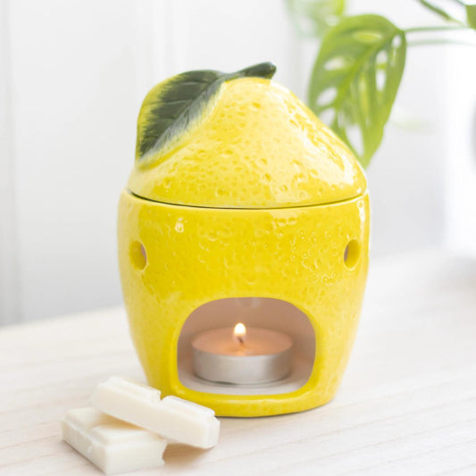 Yellow lemon-shaped candle holder with a lit tealight candle on a white surface.
