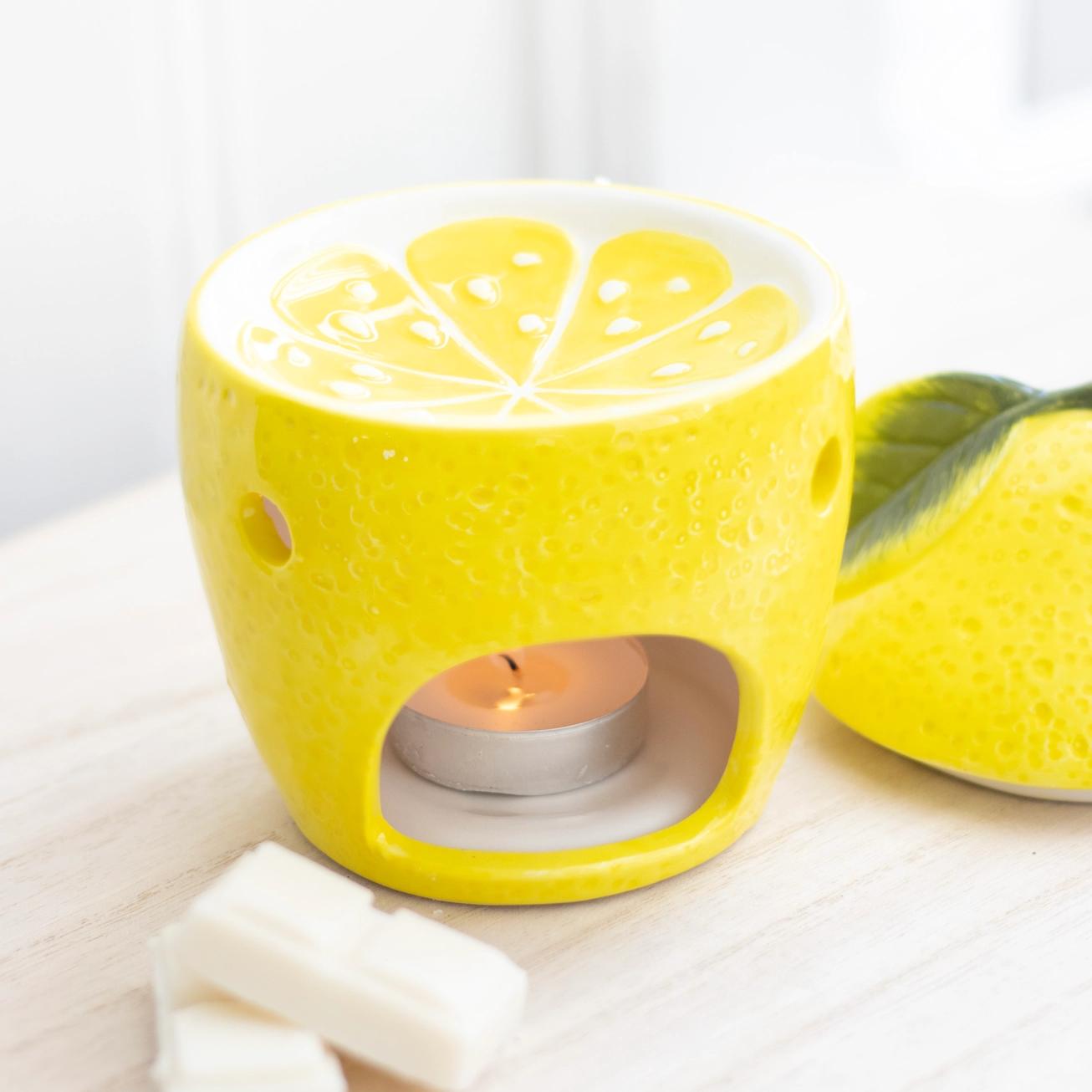Yellow lemon-shaped candle holder with a lit tealight candle on a white surface.