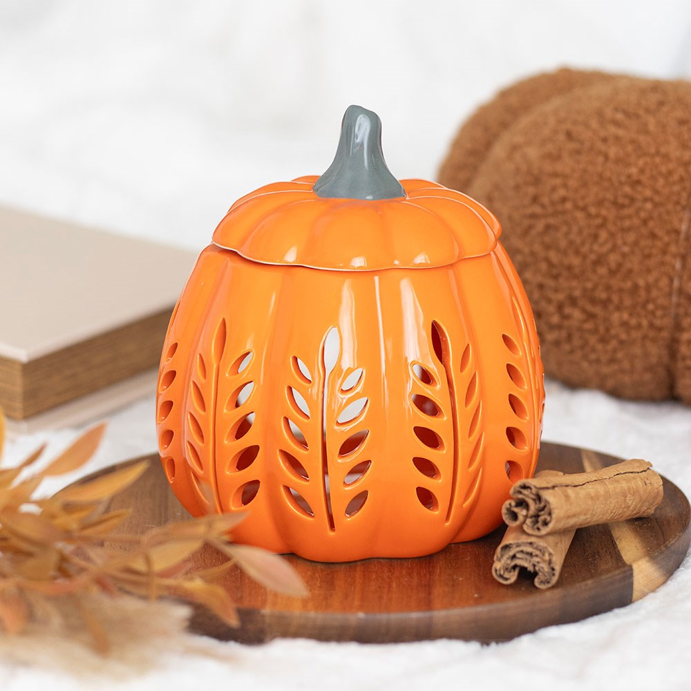 Pumpkin-shaped lantern with a lid on a wooden surface with cinnamon sticks and leaves.