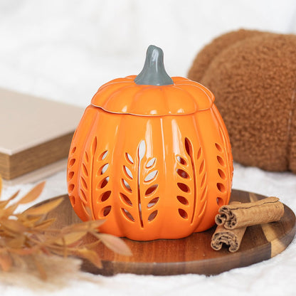 Pumpkin-shaped lantern with a lid on a wooden surface with cinnamon sticks and leaves.