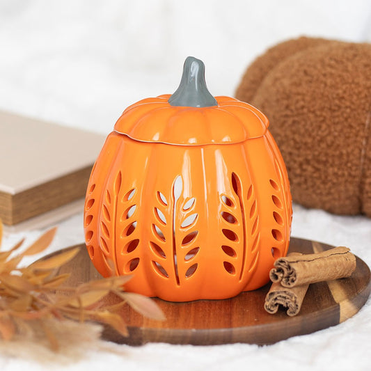 Pumpkin-shaped lantern with a lid on a wooden surface with cinnamon sticks and leaves.