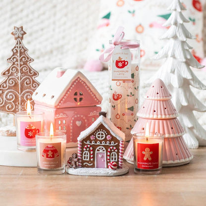 Decorative candles and gingerbread-themed items on a table with a Christmas tree in the background.