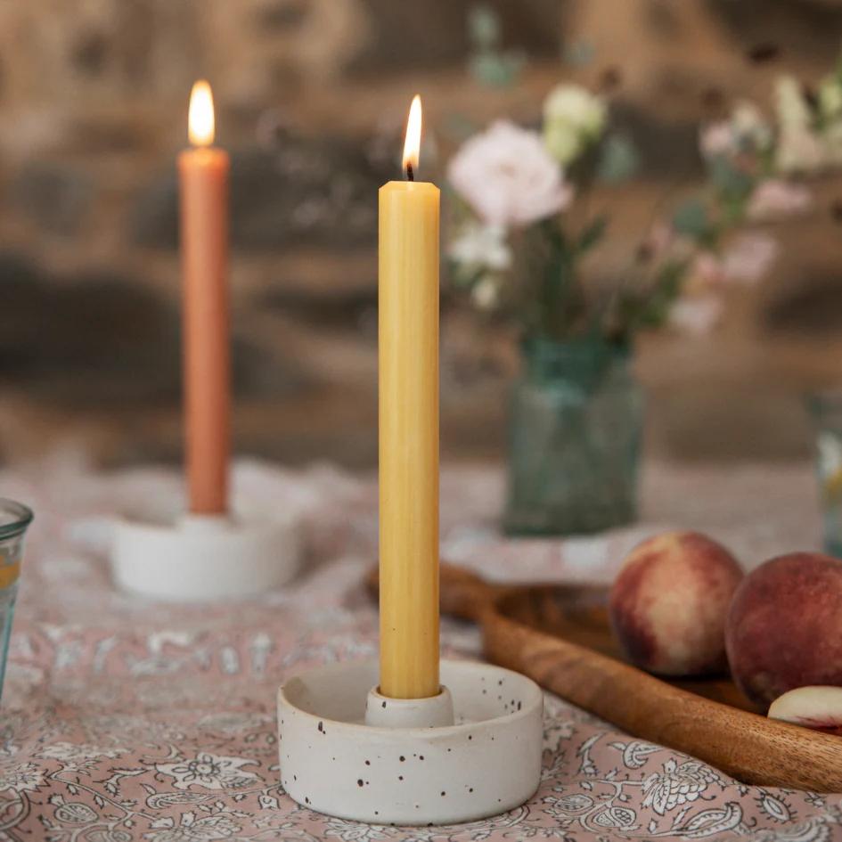 Candle in a white holder on a patterned tablecloth with peaches and flowers in the background