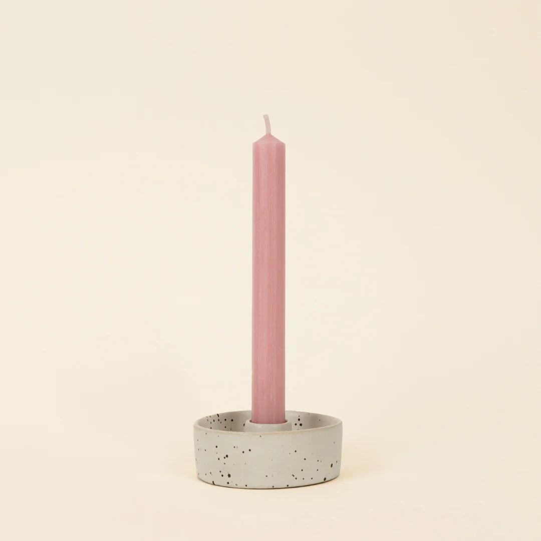 Pink candle in a speckled ceramic holder on a beige background