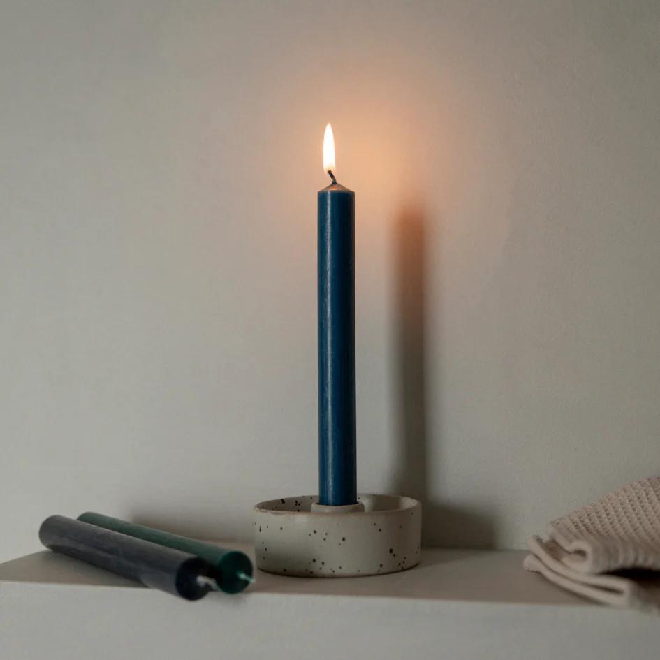 Blue candle in a concrete holder on a white surface with a neutral background