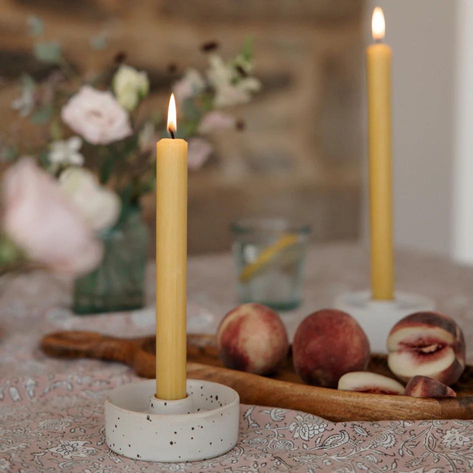 Candle in a decorative holder on a table with peaches and flowers in the background