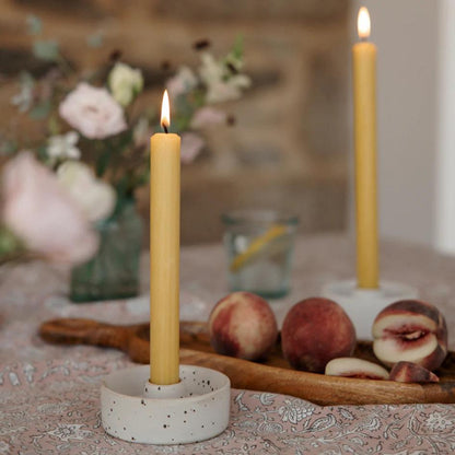 Candle in a decorative holder on a table with peaches and flowers in the background