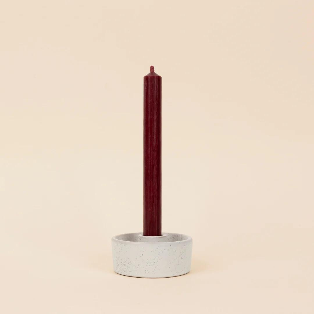 Ceramic candle holder with a red candle on a beige background