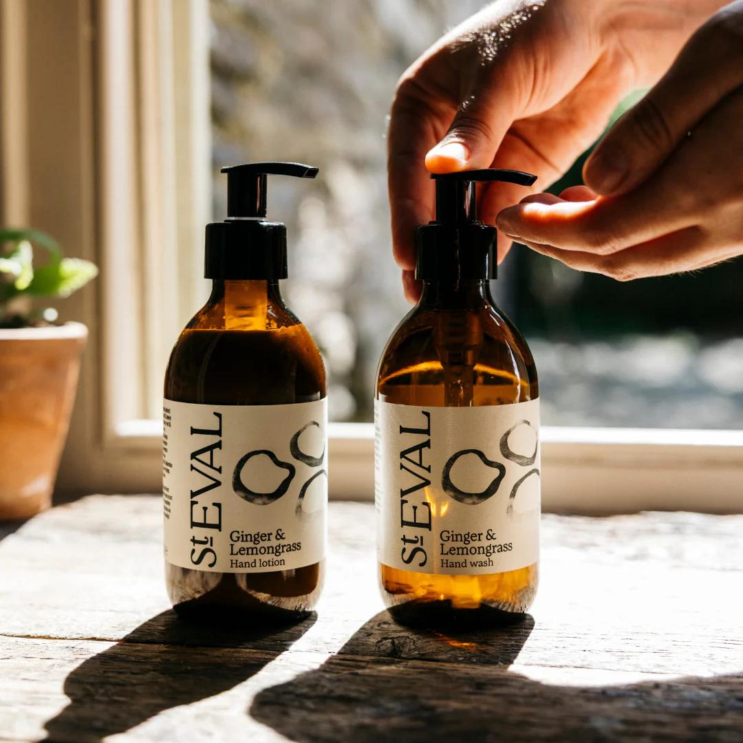 Two bottles of ST EVAL Ginger & Lemongrass hand products on a wooden surface with a blurred background.