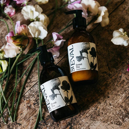 Two bottles of ST EVAL Sweet Pea products on a wooden surface with flowers.