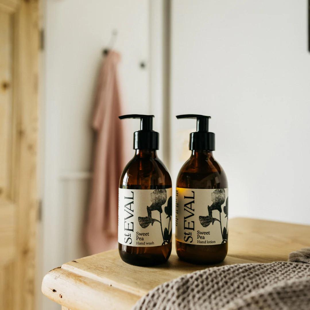 Two bottles of ST EVAL Sweet Pea Hand Wash on a wooden surface with a blurred bathroom background.