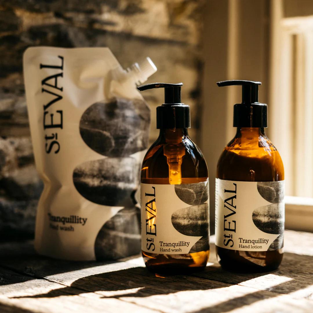 Two bottles of St. Eval Tranquility Hand Wash and Hand Lotion on a textured surface with a stone wall background.