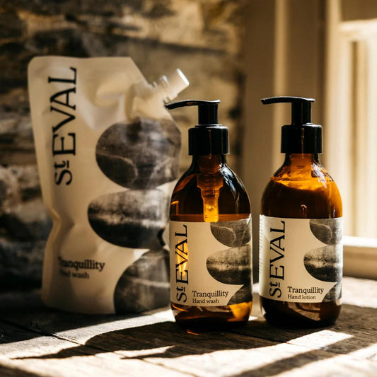 Two bottles of St. Eval Tranquility Hand Wash and Hand Lotion on a textured surface with a stone wall background.