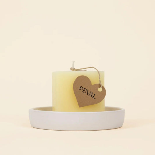Yellow candle with a heart-shaped tag labeled 'St EVAL' on a white dish against a beige background